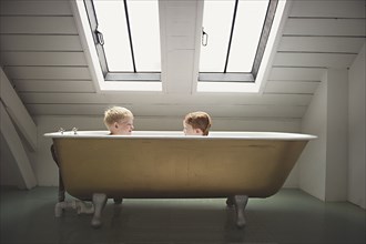 Caucasian brothers sitting in bathtub