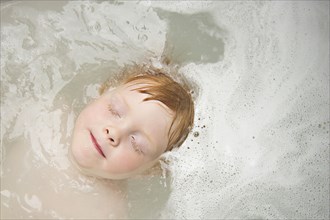 Caucasian boy with eyes closed in bubble bath
