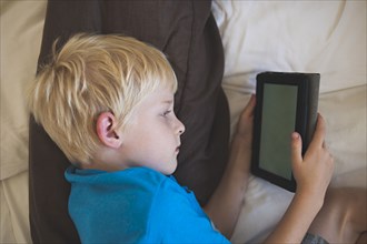 Caucasian boy reading digital tablet in bed