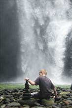 Caucasian boy stacking rocks near waterfall