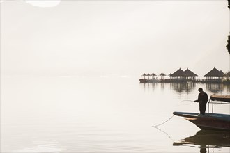 Fisherman standing in boat on still remote lake