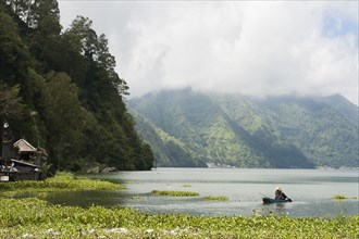 Fisherman rowing canoe on still rural lake