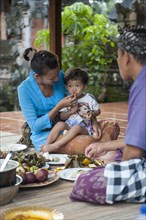Asian mother feeding son on woven mat