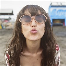 Caucasian woman in sunglasses puckering to kiss at beach