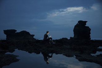 Caucasian teenage boy exploring rocky tidal pools at night