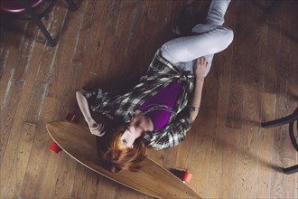 Caucasian woman laying on floor with skateboard