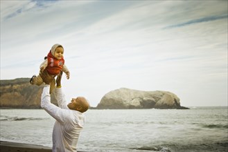 Father lifting baby son overhead at beach