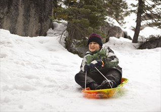 Smiling Hispanic boy riding sled in snow