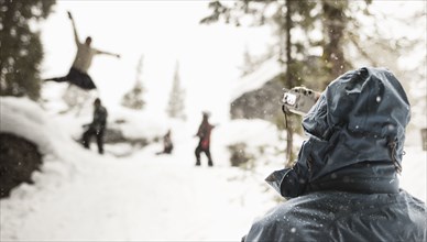 Parent with digital camera photographing kids playing in snow