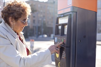 Senior Hispanic woman using parking meter