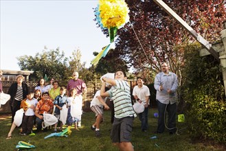 Hispanic family breaking pinata in backyard