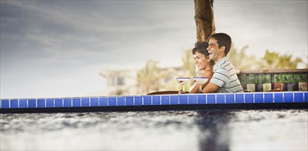 Hispanic couple drinking cocktails at poolside