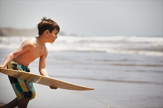 Mixed race boy holding board on beach