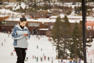 Hispanic girl text messaging on snowy slope
