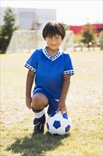 Hispanic boy with soccer ball kneeling on field