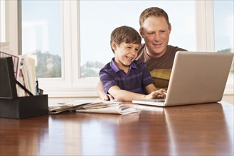 Father and son using laptop at desk