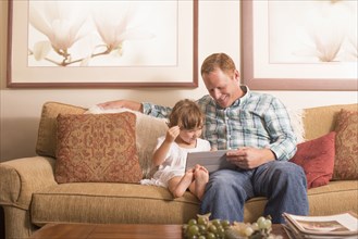 Father and daughter using digital tablet on sofa