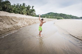 Mixed race boy playing in river on beach