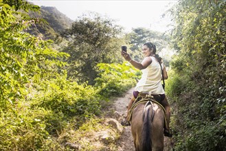 Hispanic woman taking pictures on horseback in jungle