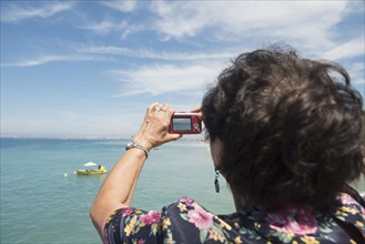 Older woman taking photograph of tropical ocean