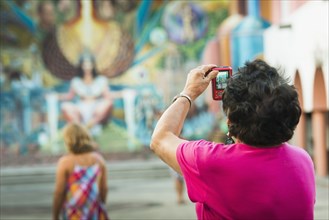 Older woman photographing urban mural
