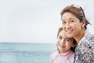 Asian mother and daughter smiling near ocean