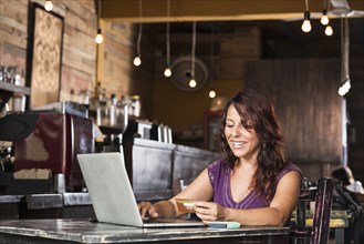 Hispanic woman shopping on laptop in coffee shop