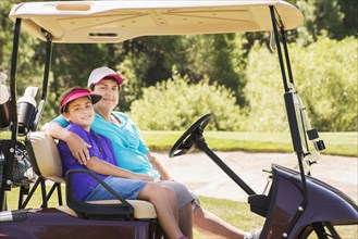 Grandmother and grandson driving golf cart on course