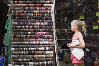 Caucasian girl admiring woven bracelets for sale in market
