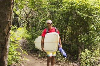 Caucasian man carrying surfboard in jungle