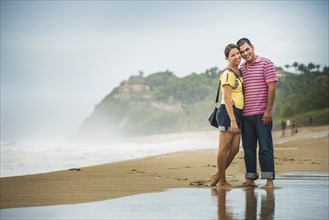 Hispanic couple hugging in waves on beach