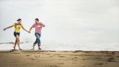 Hispanic couple running in waves on beach