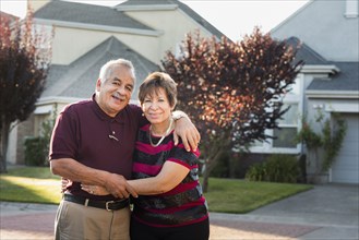 Older Hispanic couple smiling outside suburban home