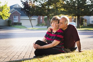Older Hispanic couple kissing outside suburban home