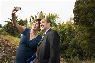 Hispanic couple taking cell phone selfie in formal wear