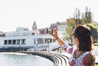 Hispanic woman taking cell phone photograph of waterfront