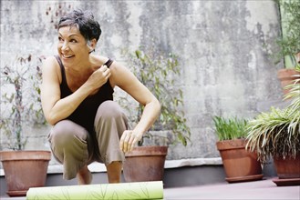 Older Caucasian woman rolling up yoga mat in courtyard