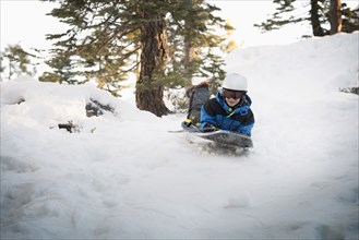 Mixed race boy sledding on snowy hillside