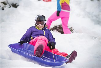 Mixed race girl sledding on snowy hillside