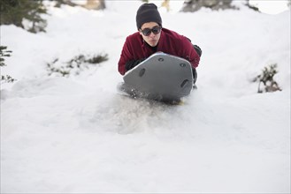 Hispanic man sledding on snowy hillside