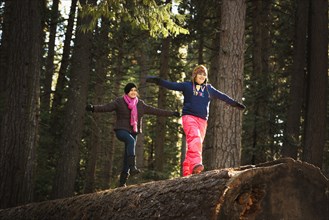 Children balancing on log in forest