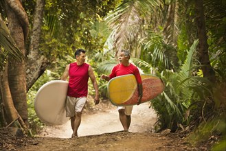 Hispanic men carrying surfboards on jungle trail