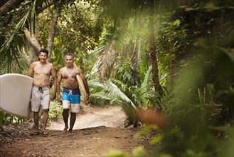 Hispanic men carrying surfboards on jungle trail