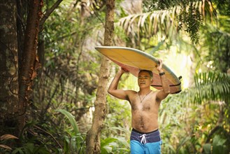 Hispanic man carrying surfboard through jungle