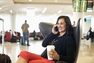 Hispanic businesswoman talking on cell phone in airport waiting area