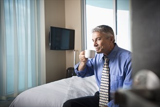 Caucasian businessman drinking coffee on hotel bed