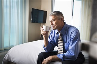 Caucasian businessman drinking coffee on hotel bed