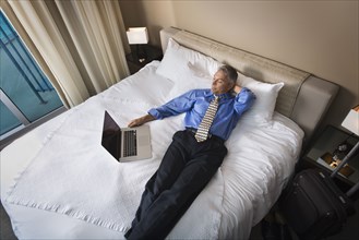Caucasian businessman using laptop on hotel bed