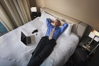 Caucasian businessman laying with laptop on hotel bed