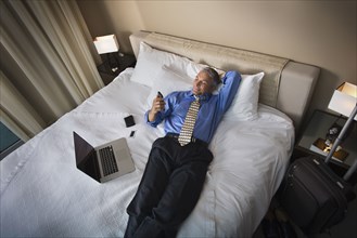Caucasian businessman using cell phone on hotel bed